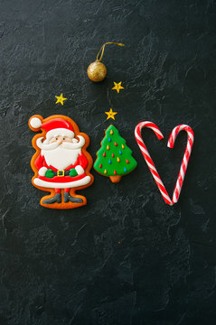 Festive Christmas background, Cookies with image of Santa, fir tree, candy canes, stars and ball on a black stone background. Top view with copy space.