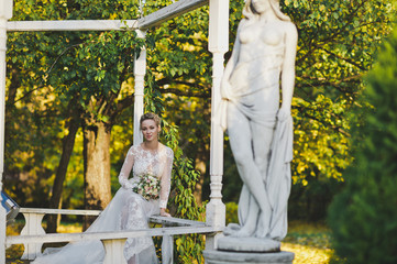 The bride resting on a bench in a beautiful garden with statues 246.