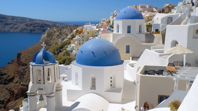 Panning view of blue dome Greek churches on the steep cliff in Santorini Island. Aegean Sea