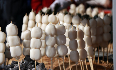 Mochi dessert in the wood stick skewer on the straw put in a circle around the cinder for toasting. Mochi is glutinous rice with a high starch content in Japanese food.