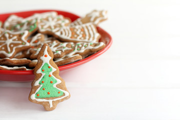 appetizing atmosphere of winter holidays/ ginger glazed cookies in the shape of Christmas tree stands on table in red plate full of different pastries