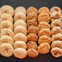 Set of various american style cookies on a black stone background. Shortbread with confetti, snickerdoodle, peanut butter, oatmeal and pecan cookies.