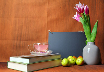 A study with books, vase of Tulips,a tea cup and a pencil stand with pencils.