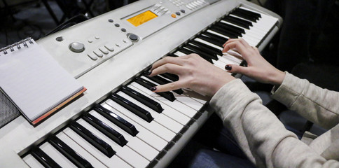 Fototapeta na wymiar A young girl pianist plays the electronic piano with her favorite music. Female graceful hands touch the keys of the synthesizer close-up.