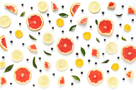 Pattern of fresh fruits on a white background, top view, flat lay.   Composition of green leaves and slices of citrus fruits: grapefruit, lemon, mandarin. Healthy food background, wallpaper, collage.