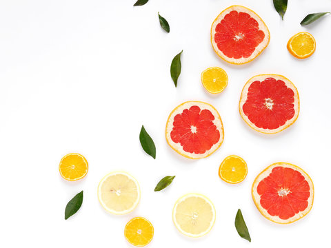 Pattern of fresh fruits on a white background, top view, flat lay.   Composition of green leaves and slices of citrus fruits: grapefruit, lemon, mandarin. Healthy food background, wallpaper, collage.
