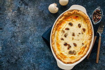 Homemade delicious quiche with mushrooms and cheese in a dish on a blue stone background. Top view with copy space.