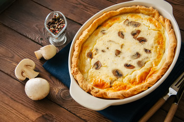 Homemade delicious quiche with mushrooms and cheese in a dish on a wooden background. Close up.
