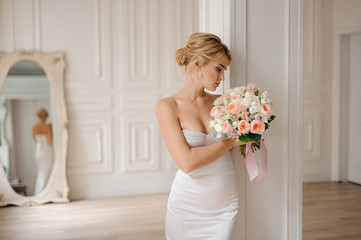 Attractive blonde bride in the elegant white dress holding a wedding bouquet