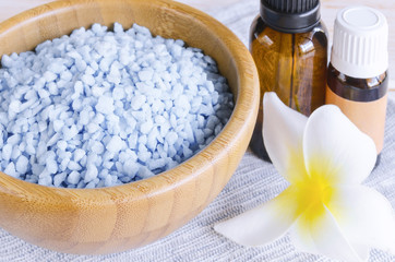 Blue spa sea salt en wooden bowl, essential oil and blue towel with exotic flower on wood background. Spa and wellness essential. Close up.