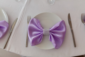 Served table plate with purple cloth. Wedding tables set for fine dining or another catered event. Napkin in the form of a bow. Plate, fork, knife on the background of the snacks on the table.