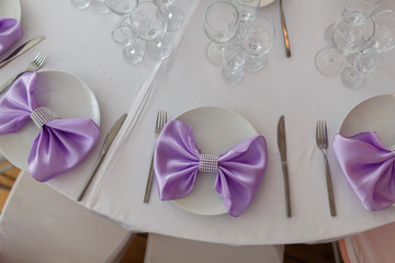 Served table plate with purple cloth. Wedding tables set for fine dining or another catered event. Napkin in the form of a bow. Plate, fork, knife on the background of the snacks on the table.