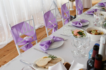 Served table plate with purple cloth. Wedding tables set for fine dining or another catered event. Napkin in the form of a bow. Plate, fork, knife on the background of the snacks on the table.