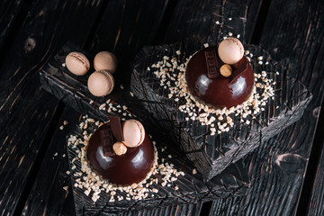 Two french chocolate mousse cake on wood background. Dessert decorated with macaroon, nut and piece...