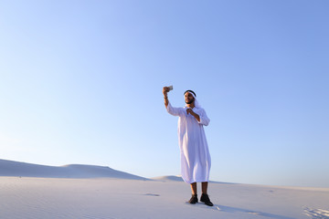 Cheerful Arab male tourist calls friend on Skype by cell and sho