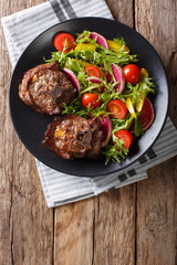 Spicy delicious lamb steak and salad from radish, tomatoes, pepper and lettuce close-up. Vertical...