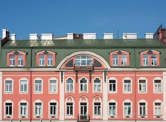 Fototapeta na wymiar Facade of an old building with a mansard roof. Windows and pink walls. Green roof and blue sky