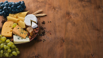 A bottle of wine, and a large assortment of cheeses, honey, nuts and spices, on a wooden table. Top view. Free space for text.