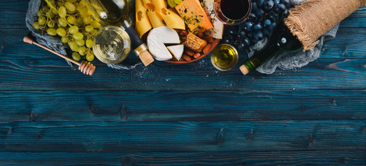 A large assortment of cheeses, wine, honey, nuts and spices, on a blue wooden table. Top view. Free space for text.