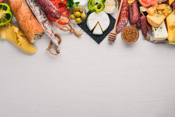Assorted cheeses and traditional sausages and vegetables on a white wooden background. Cheese brie, blue cheese, gorgonzola, fuete, salami. Italian Traditional Cuisine. Free space for text. Top view.