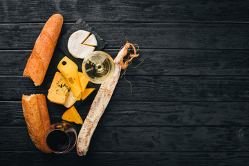 A bottle of wine, cheeses and traditional sausages on a wooden background. Brie cheese, blue cheese, gorgonzola, fuete, salami. Free space for text. Top view.