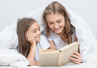 Young mother and daughter reading a book on the bed