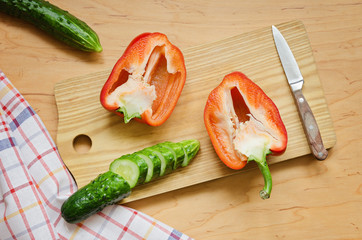 Two halves of red pepper and chopped cucumber on the kitchen boa