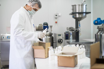 Cosmetics fabric worker taking one liquid soap from a row and putting in a paper box for transport.