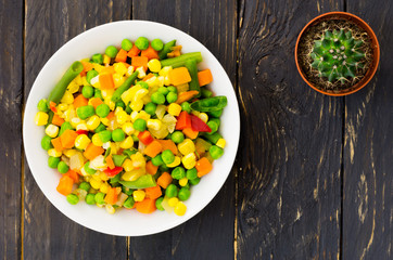 A plate with Mexican salad and a cactus on a black background. A colorful salad. Top view.