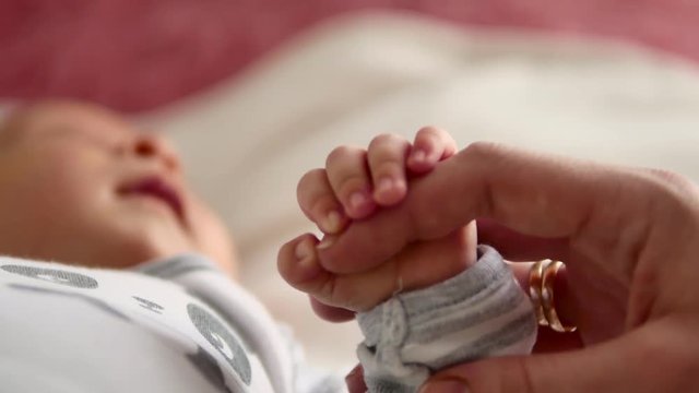 Mother and her newborn baby, parent holding newborns hand, happy mother and baby together. Maternity and parenthood concept.