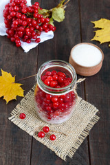 Red juicy berries of a viburnum with sugar in a glass jar on a dark wooden background. For making jam, tea. Medicinal plant.
