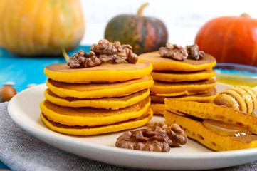 Fragrant golden pumpkin pancakes with honey and walnuts on a blue wooden background. Traditional American dish
