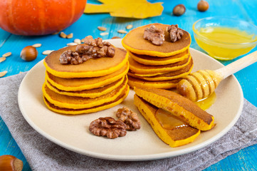 Fragrant golden pumpkin pancakes with honey and walnuts on a blue wooden background. Traditional American dish