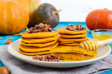 Fragrant golden pumpkin pancakes with honey and walnuts on a blue wooden background. Traditional American dish