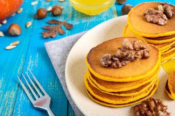 Fragrant golden pumpkin pancakes with honey and walnuts on a blue wooden background. Traditional American dish