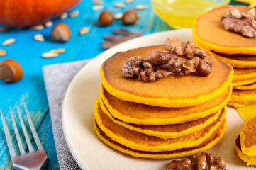 Fragrant golden pumpkin pancakes with honey and walnuts on a blue wooden background. Traditional American dish