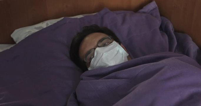 A sick man in a white mask lies in bed in the clinic during an infection. Epidemic.