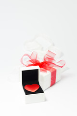 A red velvet heart in a white jewelry box and a white gift box with red ribbon on white background.