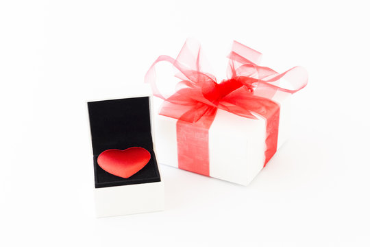 A red velvet heart in a white jewelry box and a white gift box with red ribbon on white background.