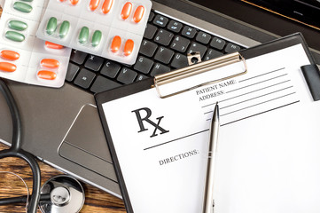 Prescription form with stethoscope and pills on the laptop keyboard.