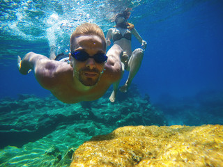 Underwater close photo of a young playful love couple swimming in the turquoise exotic sea for summer vacation.