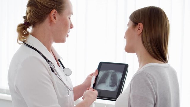 Woman physician with stethoscope talking with female patient in clinic. Female professional doctor at work. Showing X-ray on tablet. Health care