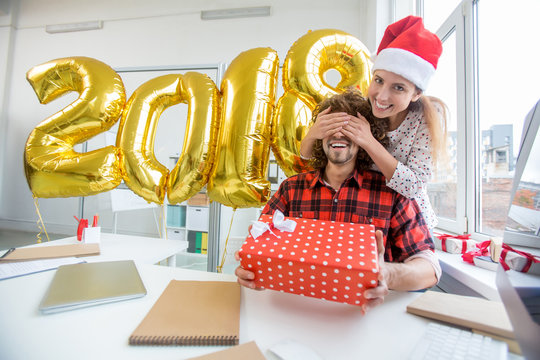 Happy guy holding giftbox while his gilfriend keeping her hands on his eyes