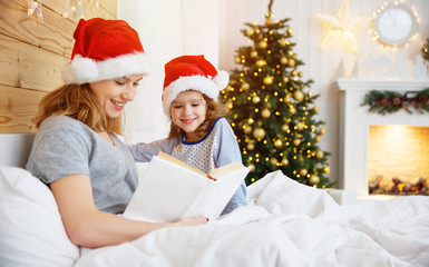 family mother reads book to child in bed on Christmas morning