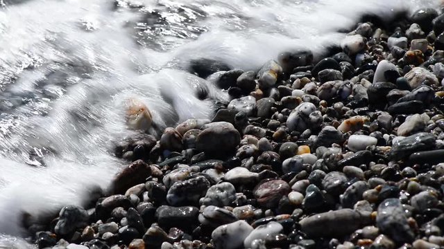 le onde del mare smuovono riflessi e sassi sulla battigia