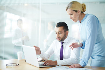 Young and mature colleagues discussing online presentation or financial data