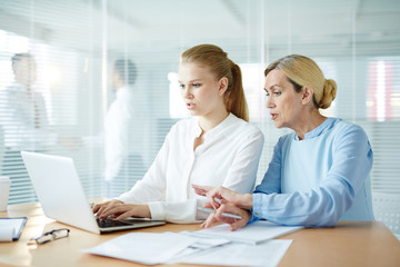 Mature employer explaining her young subordinate how to make report for conference