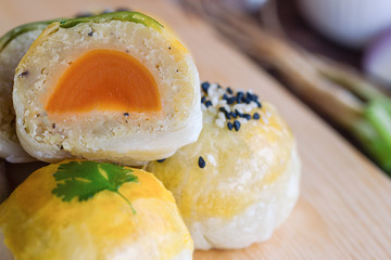 Chinese pastry or moon cake filled with mung bean paste and salted egg yolk decorated with sesame and coriander on wood cutting board in close up view, macro style. Homemade bakery concept.
