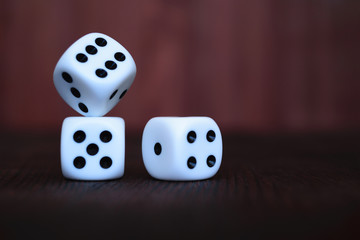 Heap of three white plastic dices on brown wooden board background. Six sides cube with black dots. Numbers 1, 2, 3, 4, 5, 6.