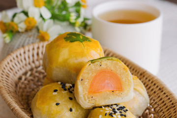 Delicious Chinese pastry or moon cake filled with mung bean paste and salted egg yolk on wood basket served with tea on wood table in side view, close up. Homemade bakery concept.